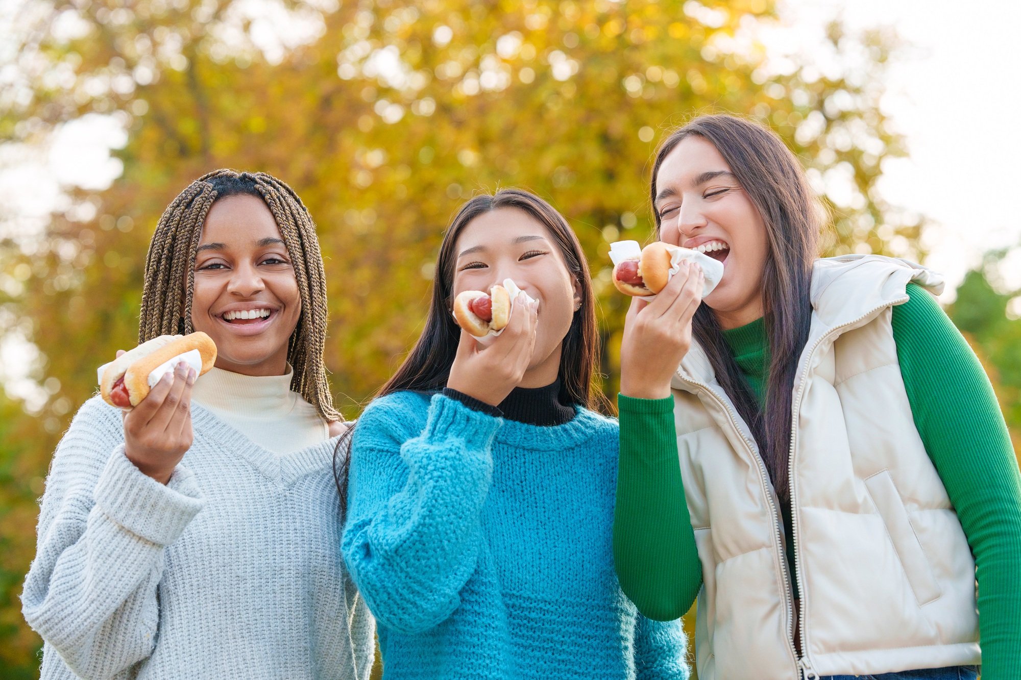 Multiethnic friends joking while eating hot dog in a park