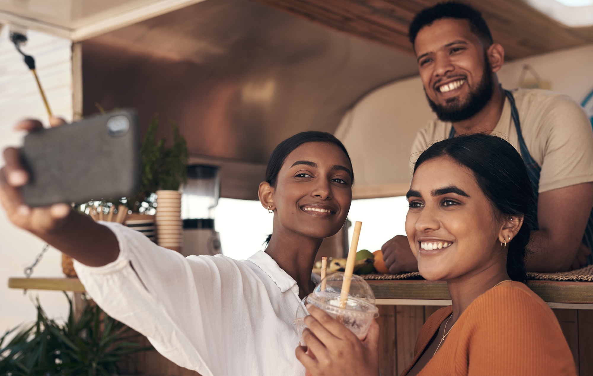Now give me a big smile. Shot of two friends taking selfies while drinking smoothies.