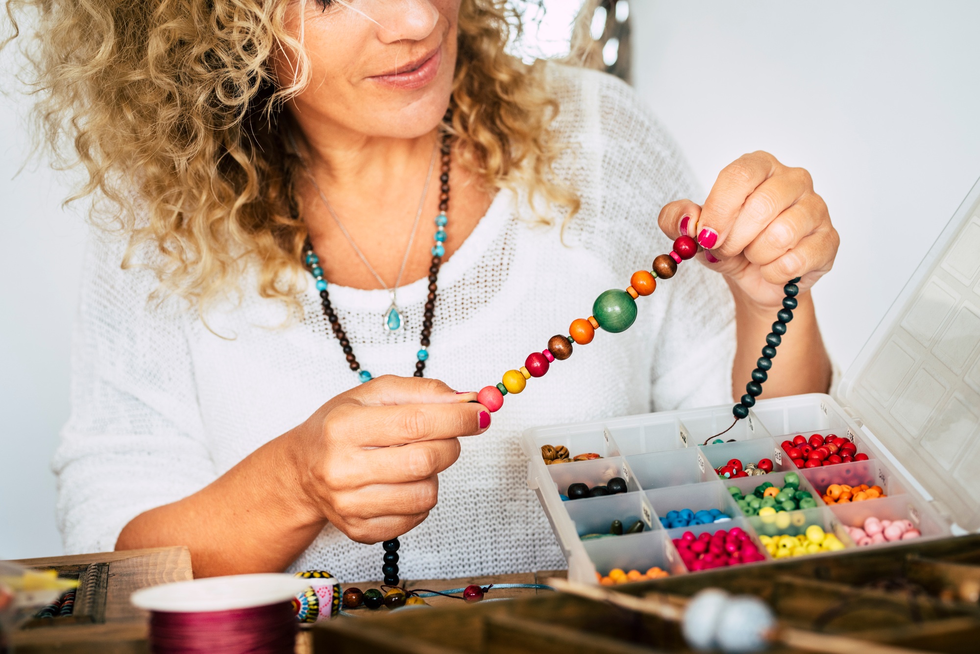 Portrait of adult woman creating beads bracelets and necklace at home for new modern business