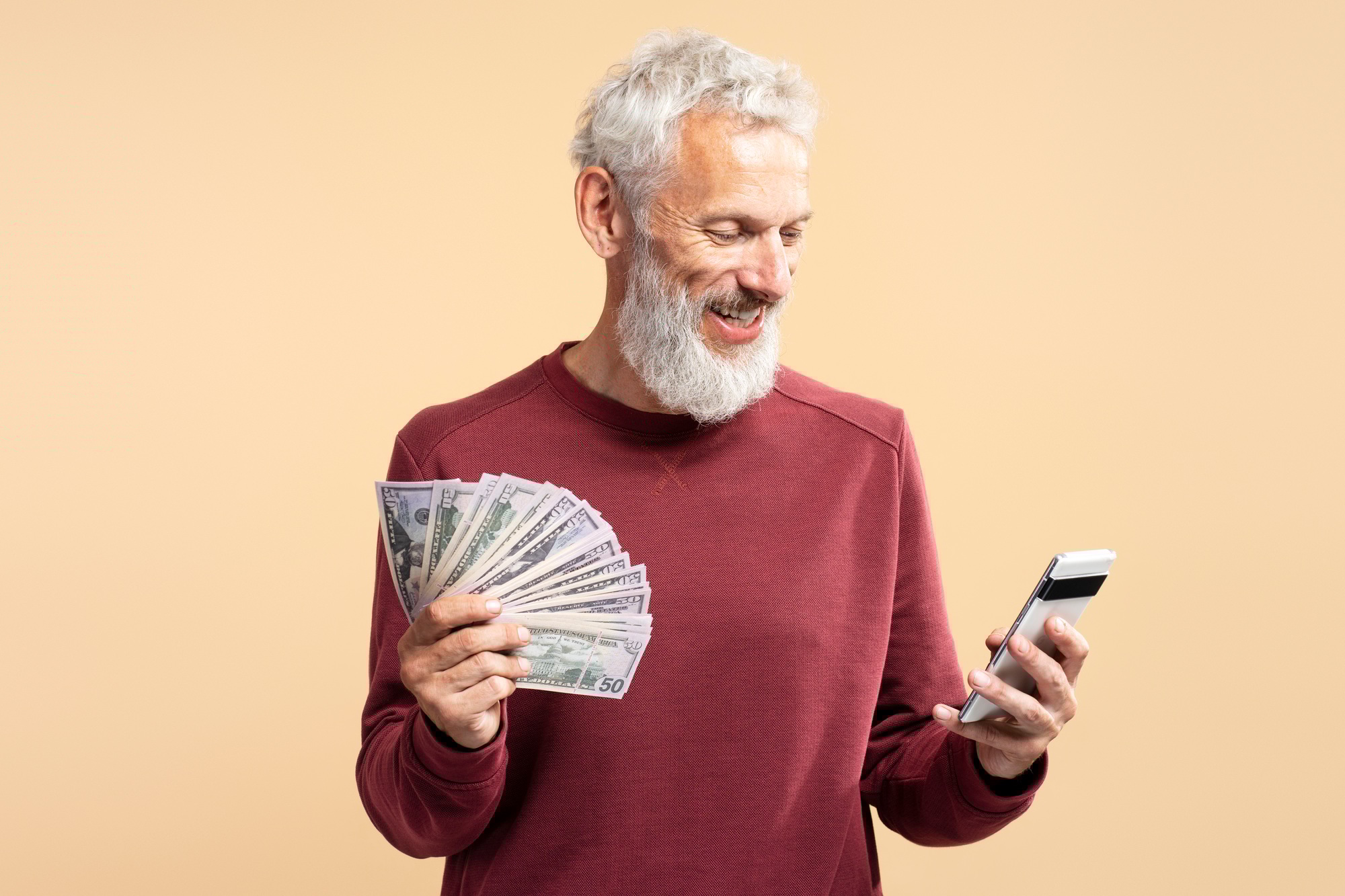 Portrait of successful smiling mature man holding money, cash and mobile phone, using mobile banking