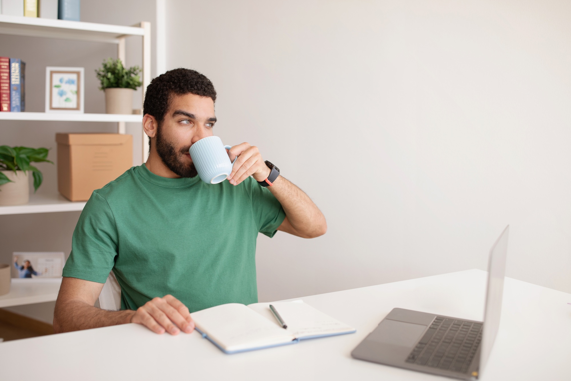 Positive millennial arab guy planning startup business at computer, drink cup of tea, enjoy coffee