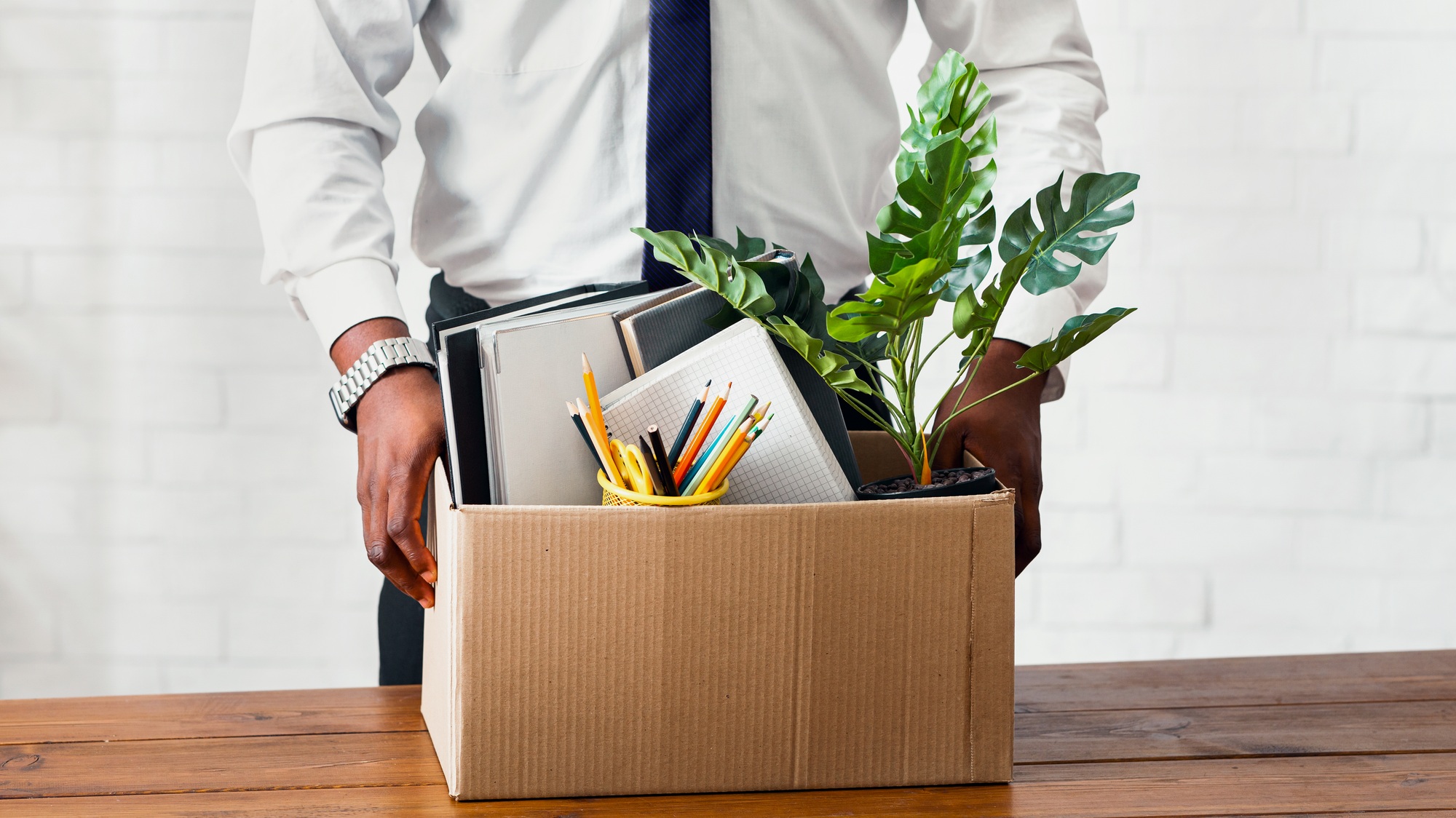 Quitting job concept. Unrecognizable African American employee with box of his belongings at office