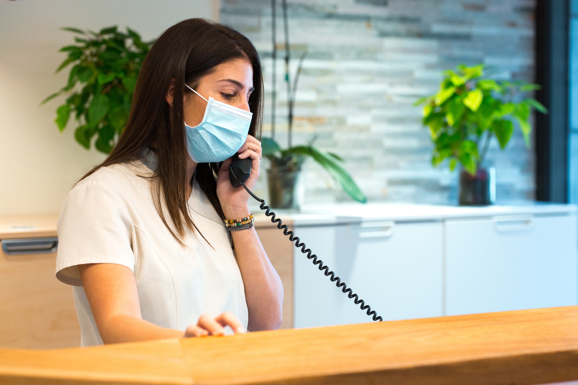 Receptionist wearing a face mask takes a call while working at a reception desk