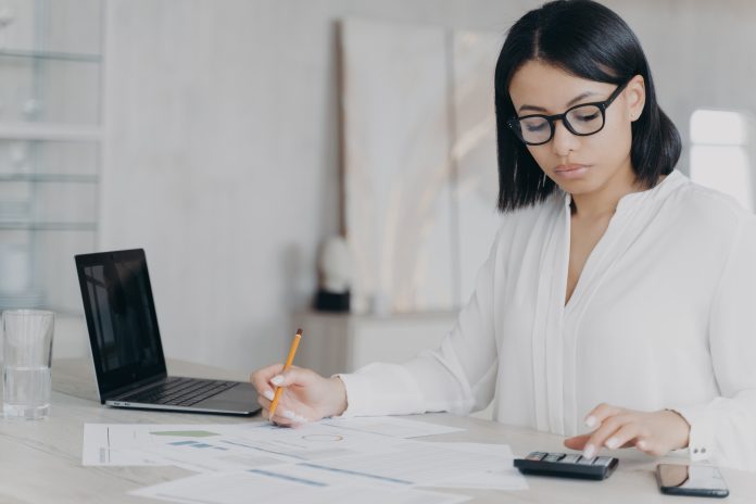 Remote accountant is calculating profit. Young hispanic bookkeeper is working distantly from home.