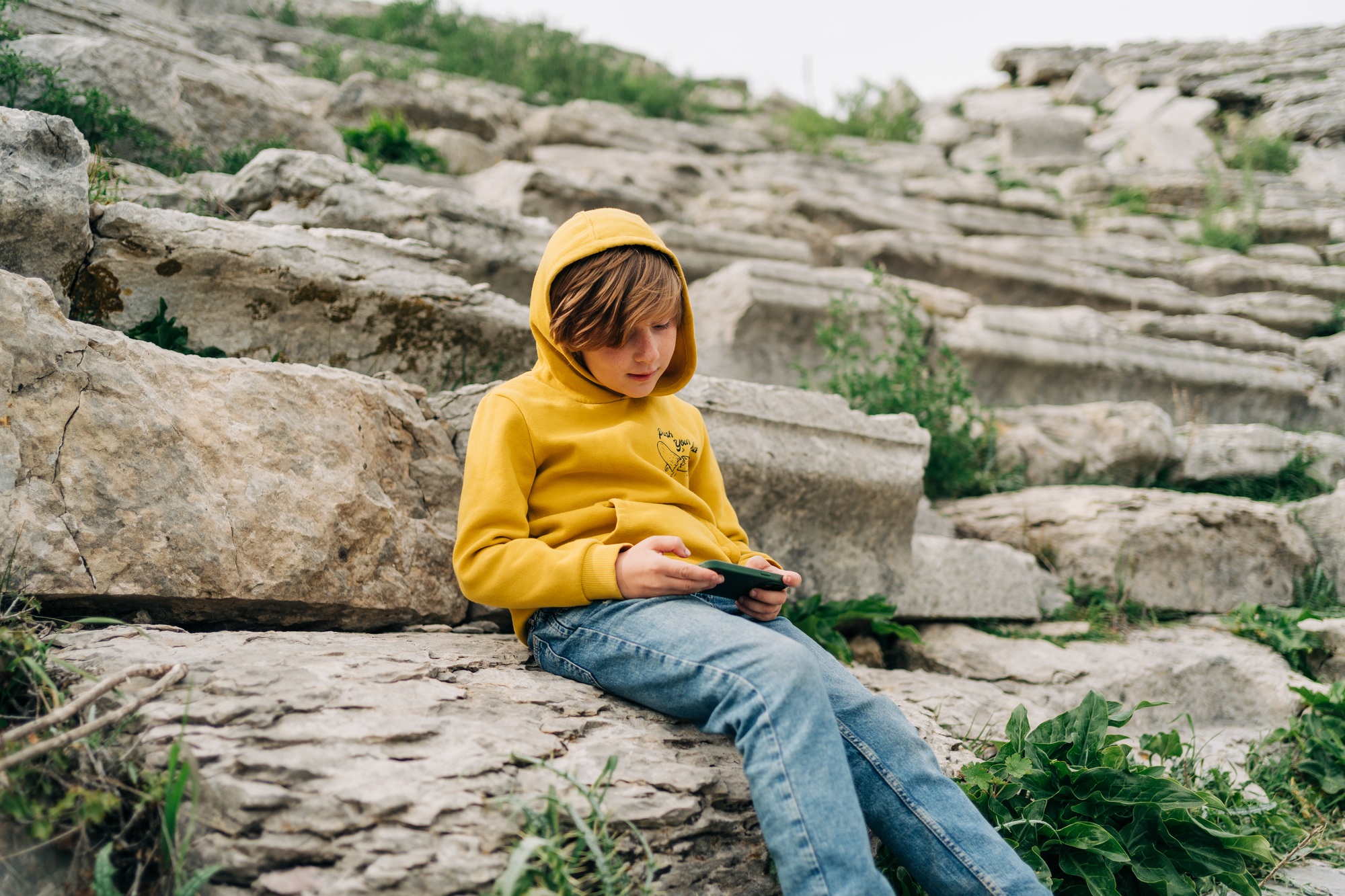 School kid child playing with his cellphone smartphone in an ancient stone amphitheater. Boy in