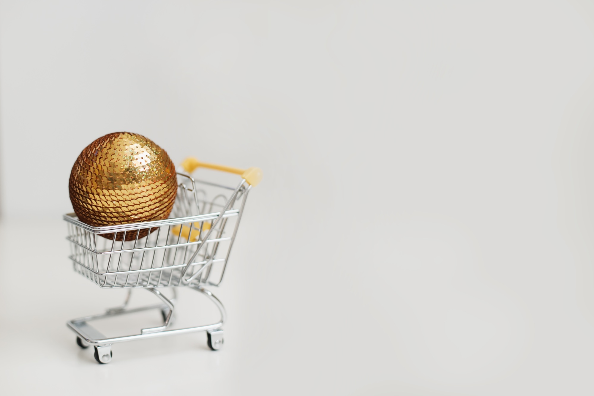 Small shopping cart with christmas ball on white background. New Year and Christmas sale or shopping