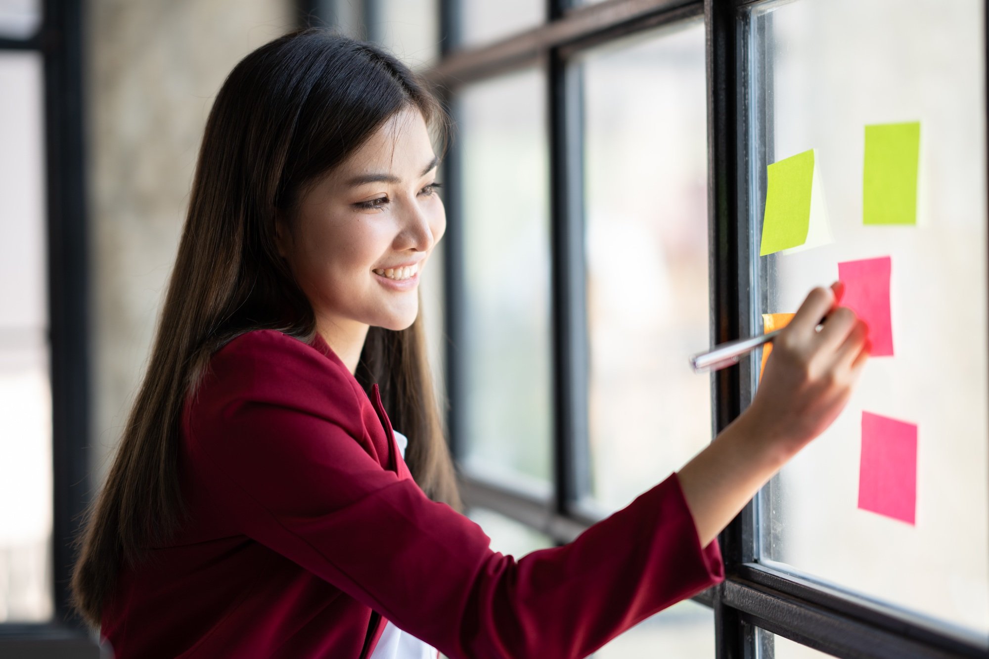Smart asian business woman mentor coach leader writing idea or task on post it sticky notes on glass