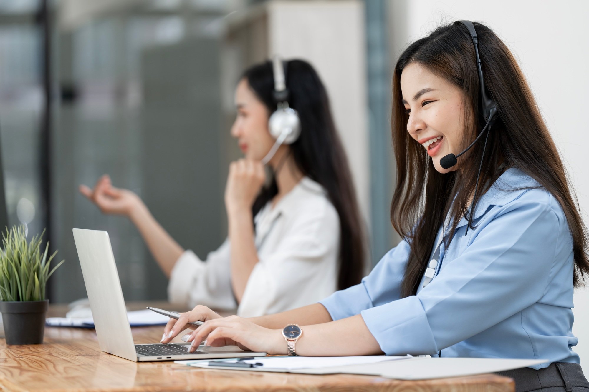 Smiling caucasian business woman with headset working on a laptop in a call center on the line.
