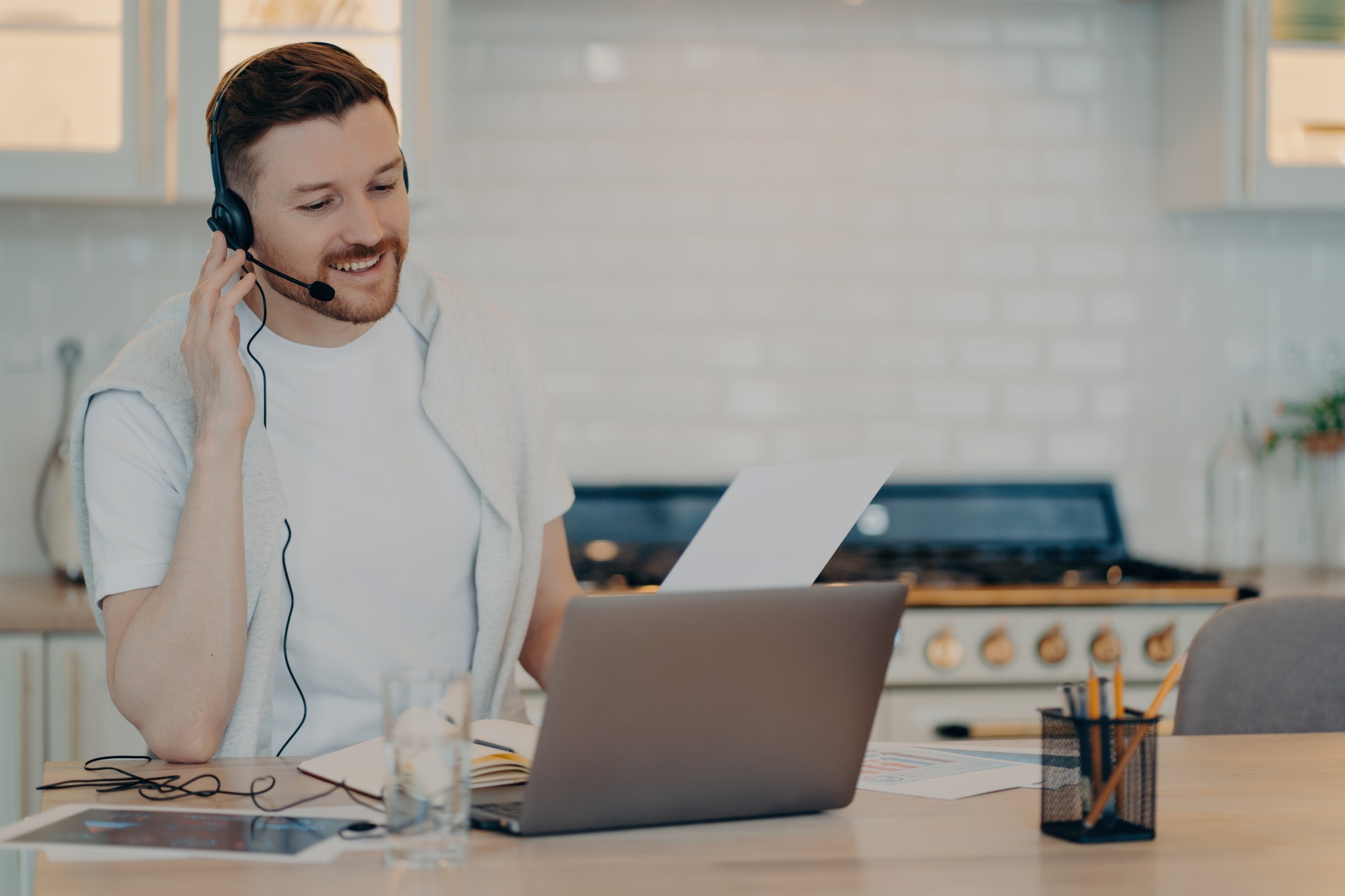 Smiling man teleworking in a casual setup with a headset, experiencing the ease of a home