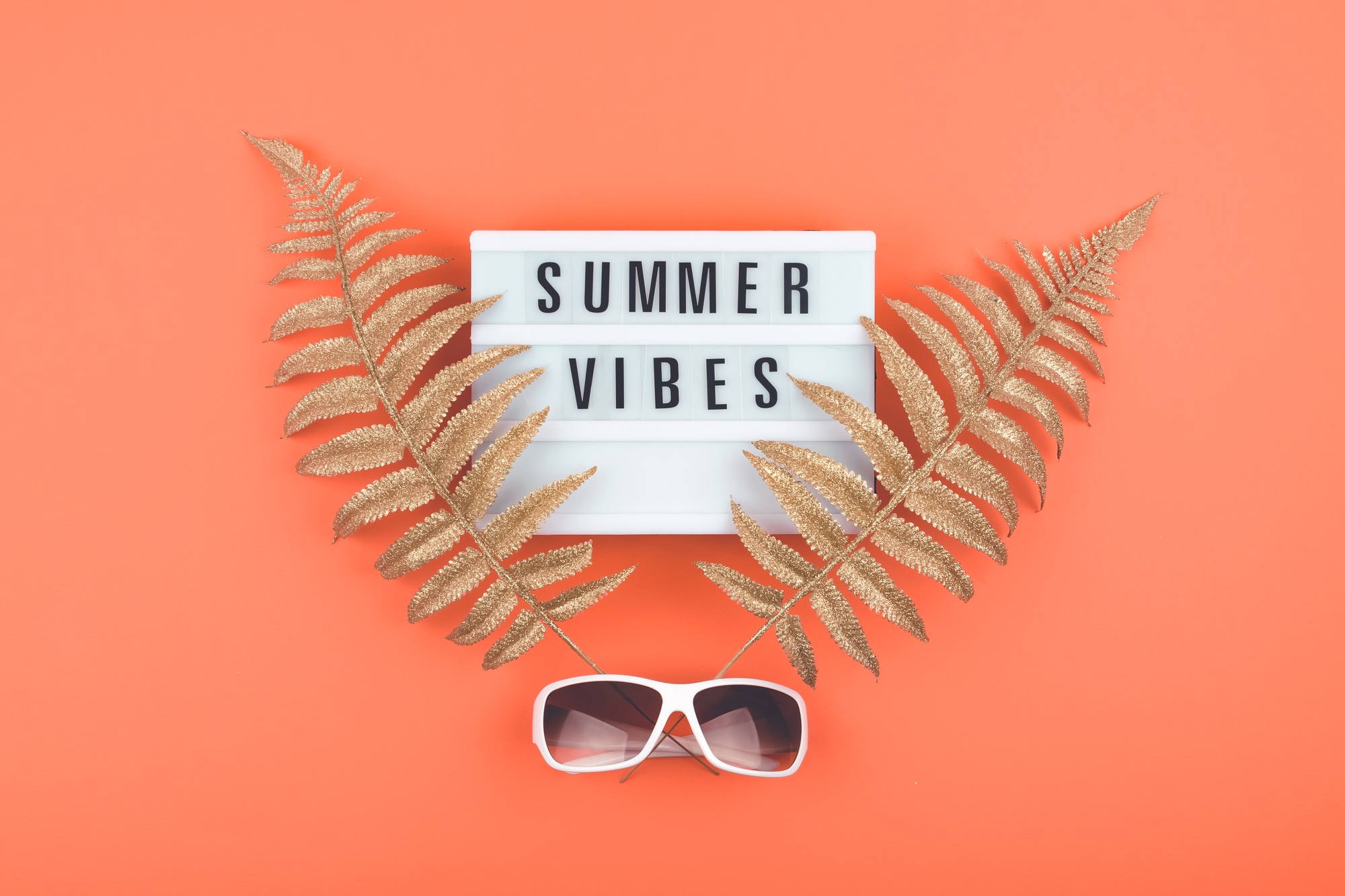Summer luxury flat lay on coral background with Summer vibes text on light box, golden tropical