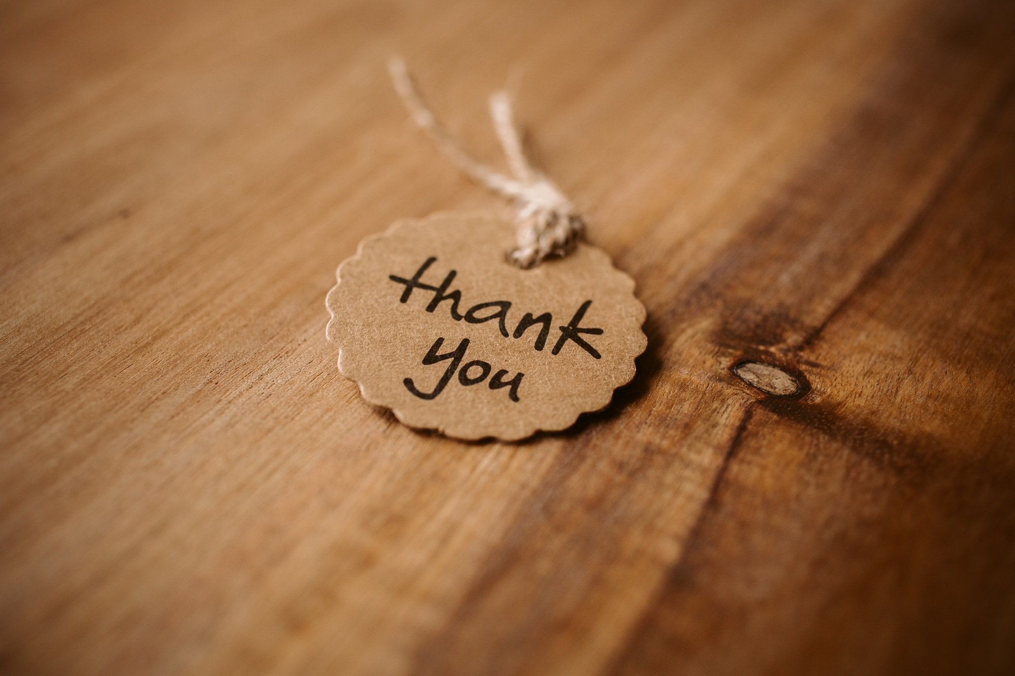 Thank you word written in a card on wooden background with selective focus.