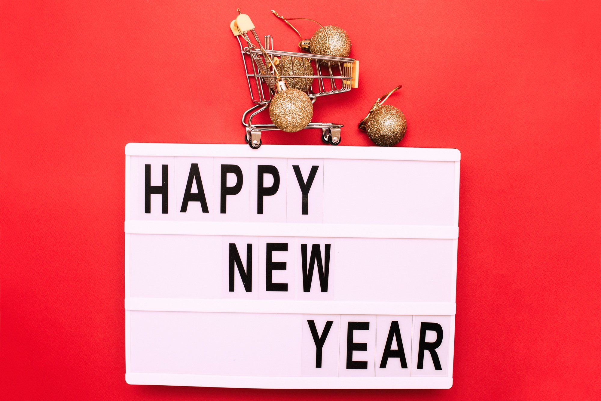 The inscription happy new year with shopping trolley with shiny gold christmas toys balls
