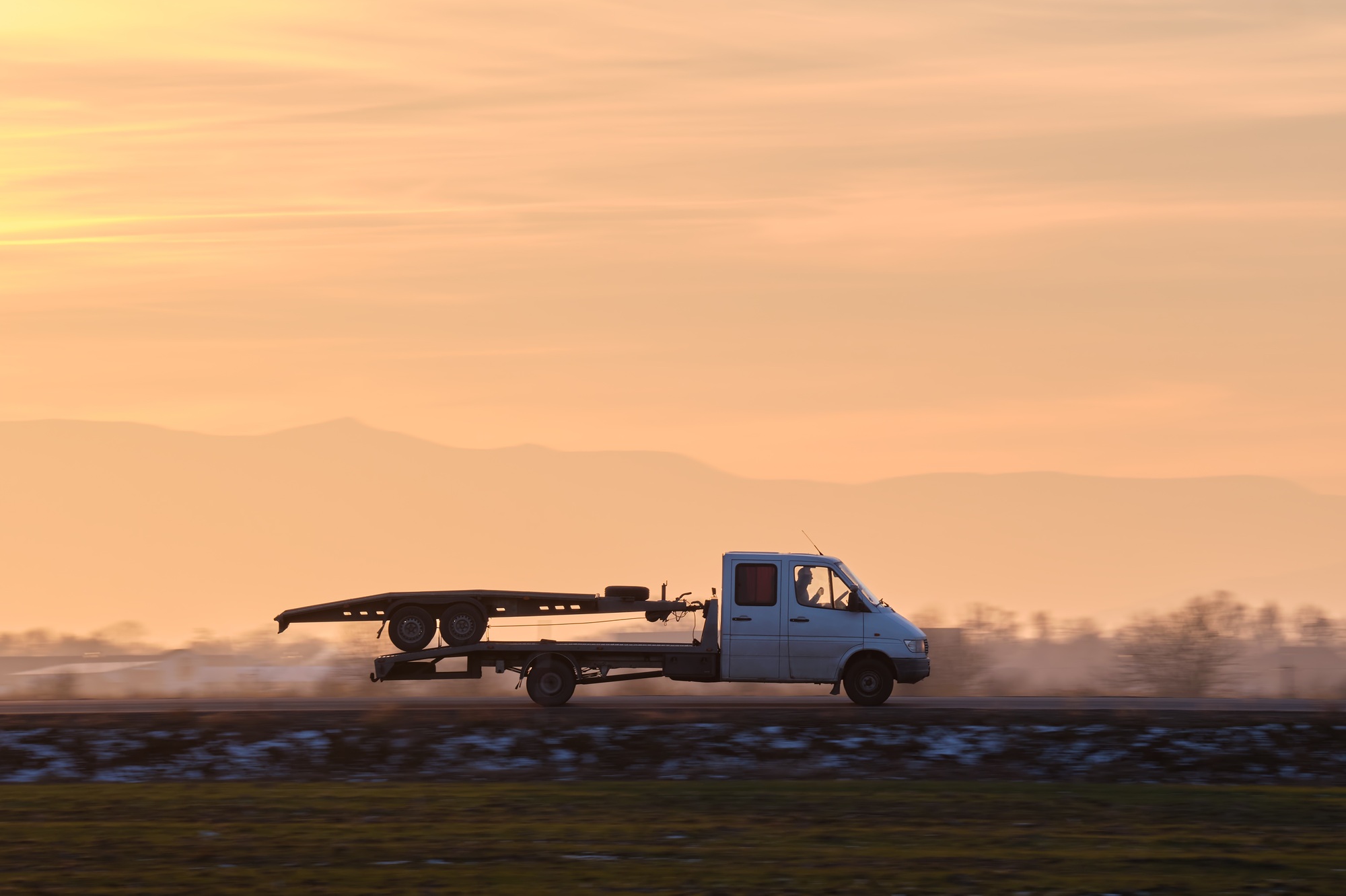Tow truck vehicle with car transporting carrier trailer driving on highway in evening
