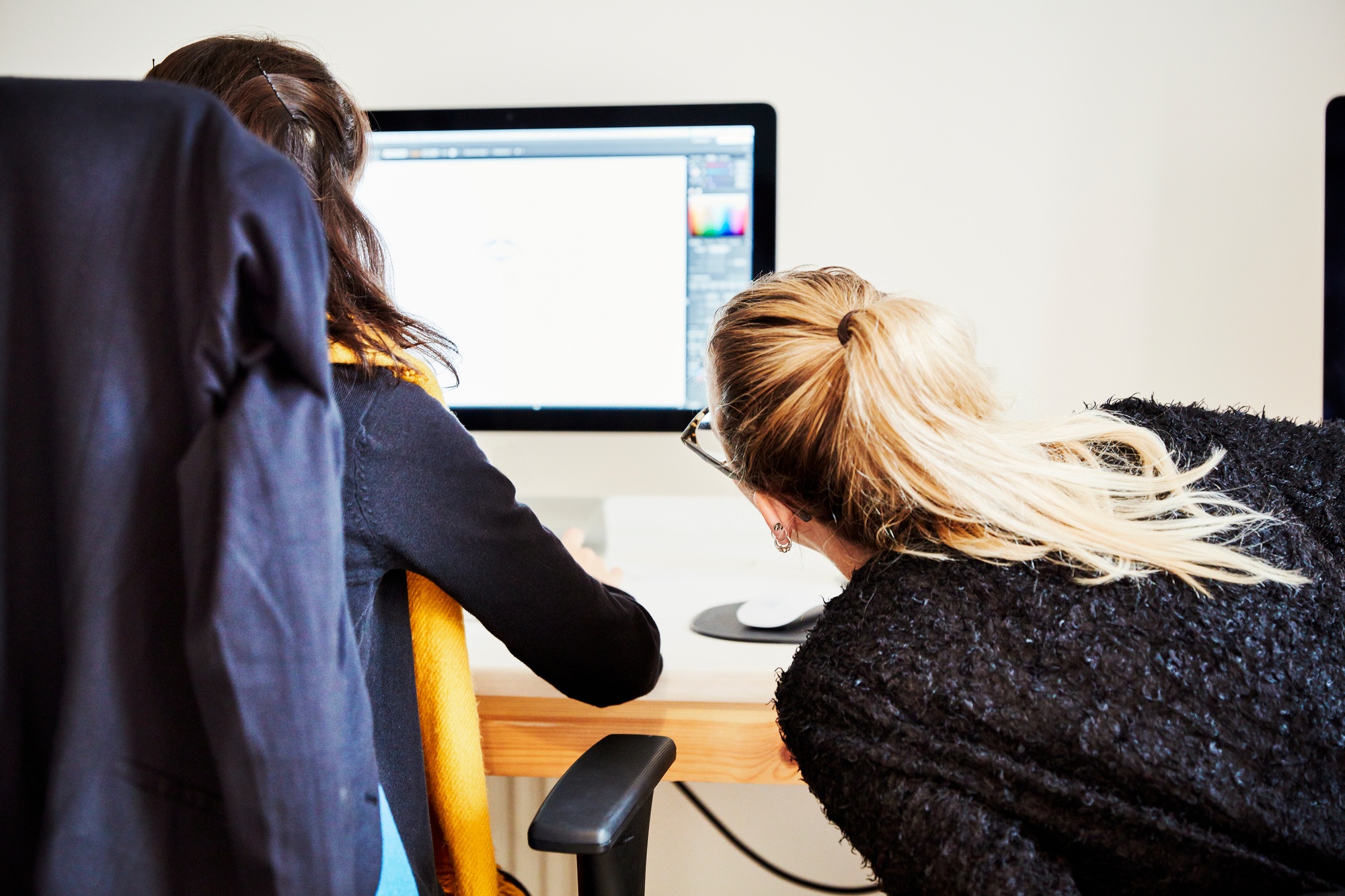 Two women seated sharing a computer screen and discussing the graphic content.