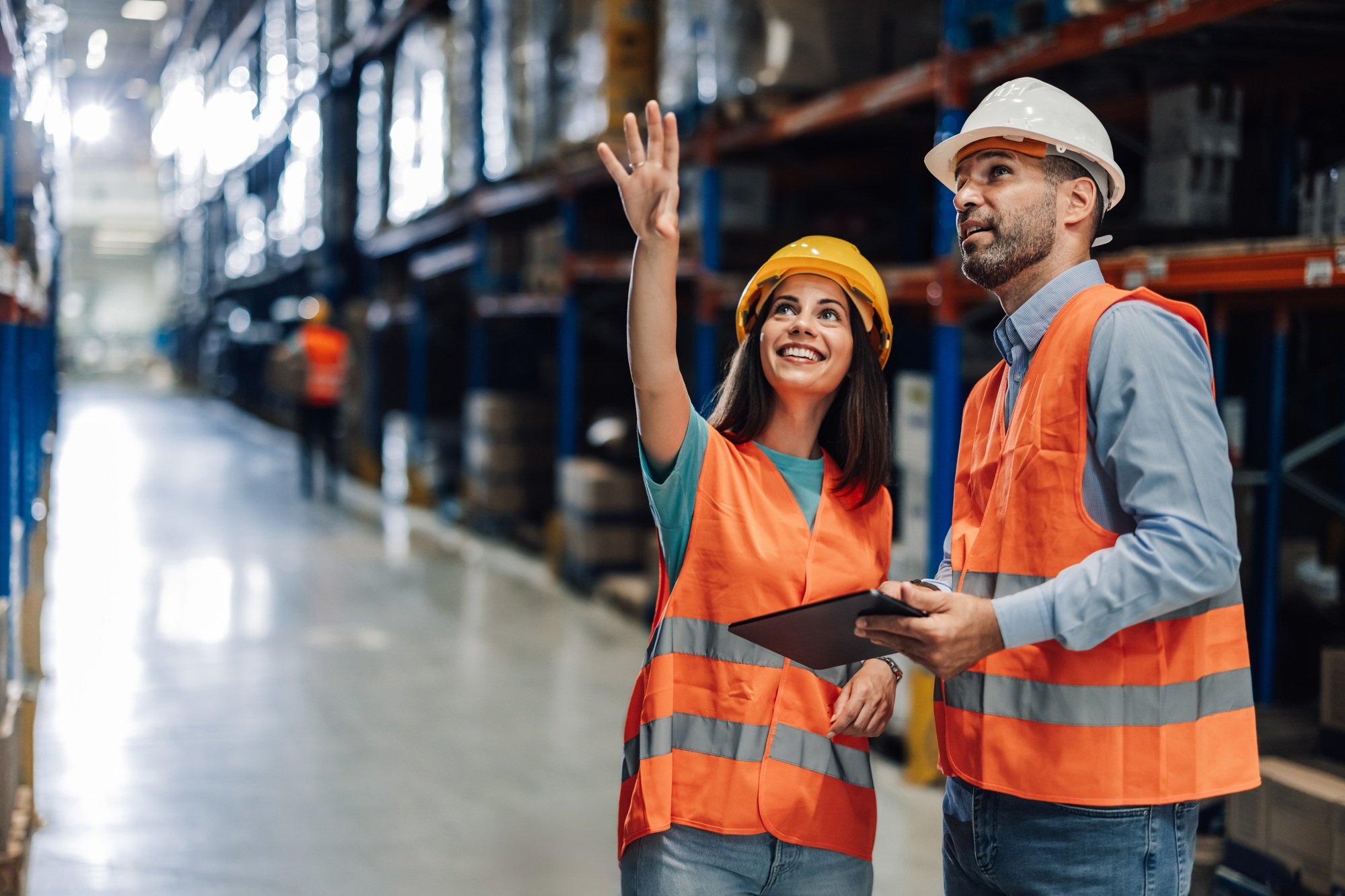 Warehouse workers discussing logistics and pointing at storage racks