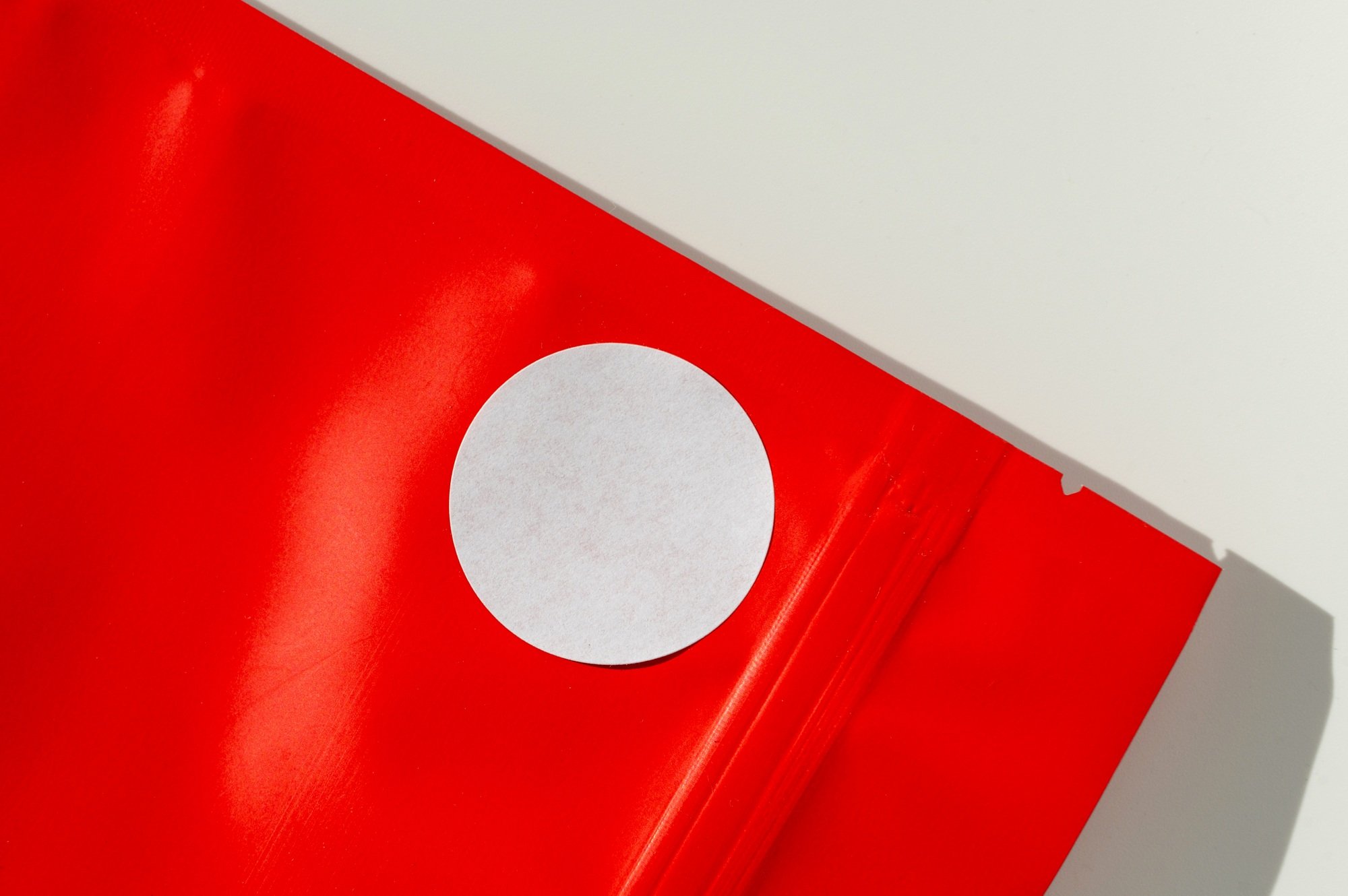 White circular sticker on red poly mailer envelope with natural shadow.
