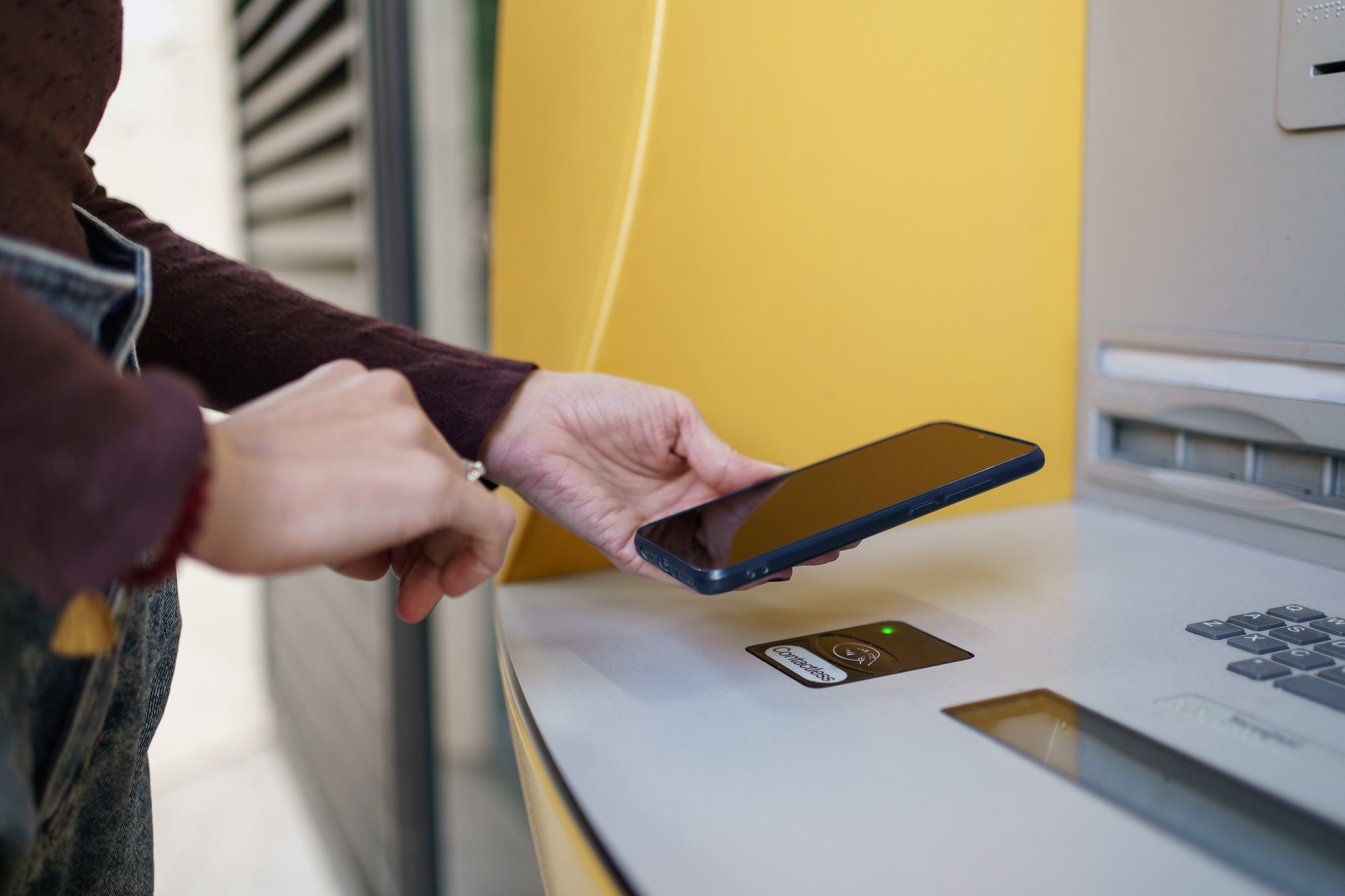 Woman hand using ATM machine to withdraw money with wireless contactless phone app