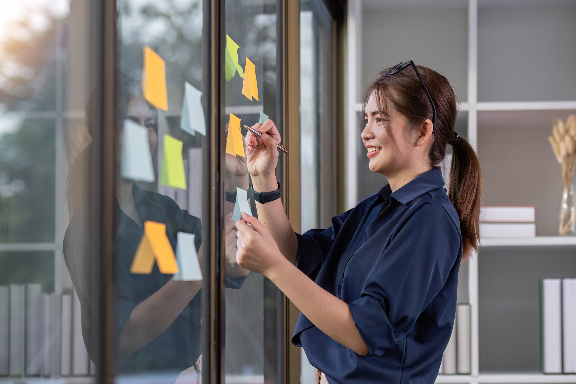 Young businesswoman writes down work plans on notes posted on the wall in the office.