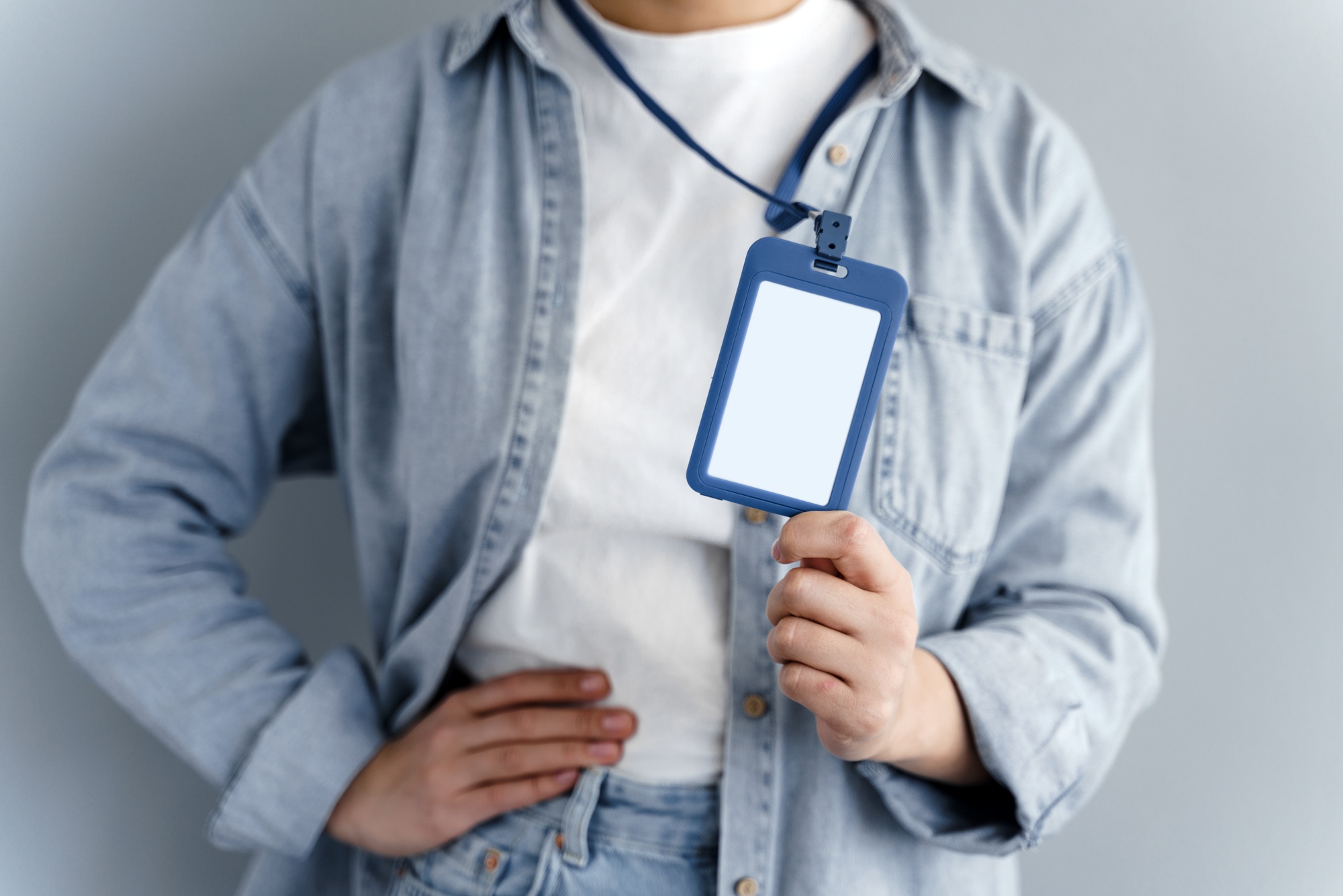 Young caucasian girl showing name tag on gray background. Close view, blank name tag.
