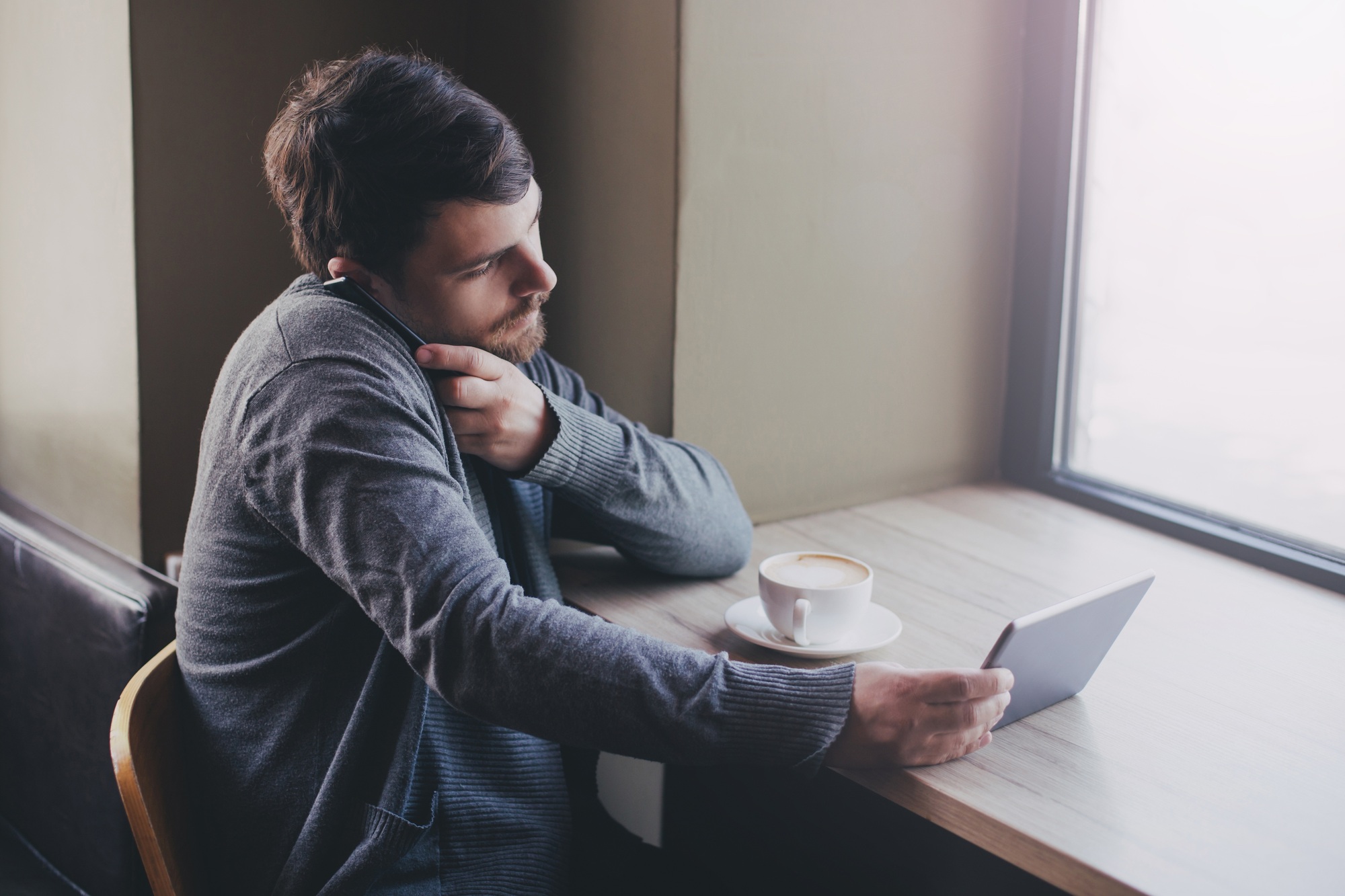 Young man drinking coffee and using his tablet and smart phone. Business and marketing concept.