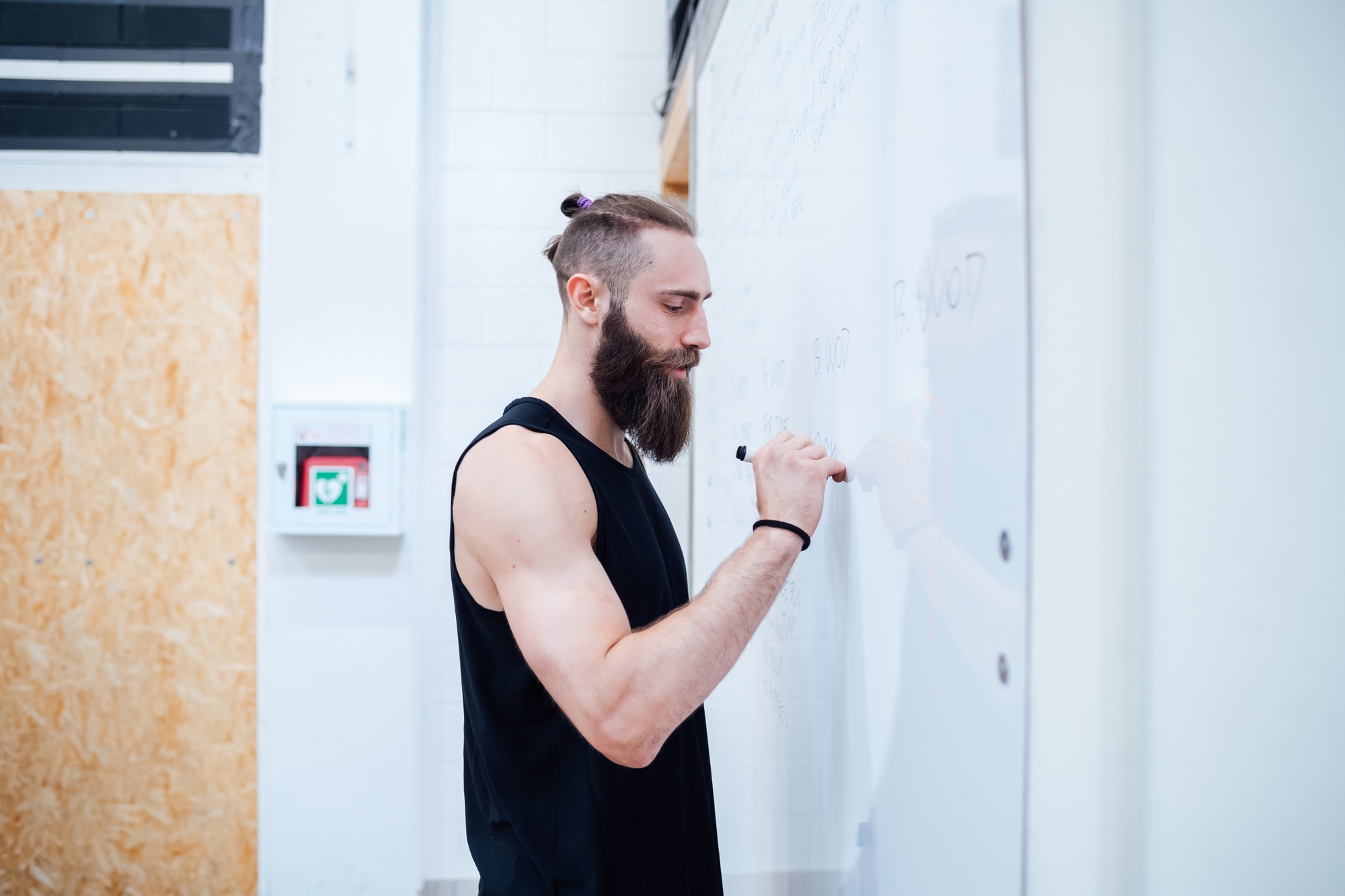 Young man personal trainer indoor gym writing on whiteboard planning training