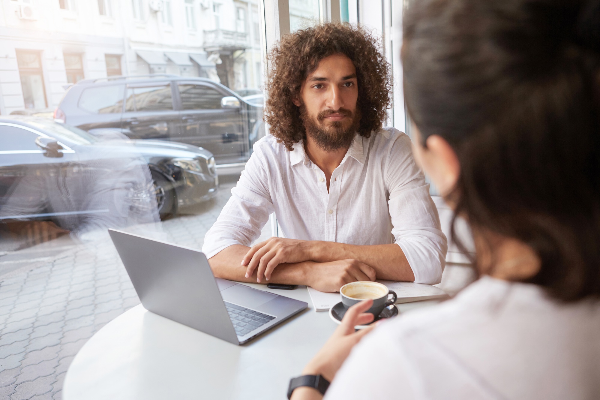 young pretty man with beard having business meeting in luncheonette, sitting near window