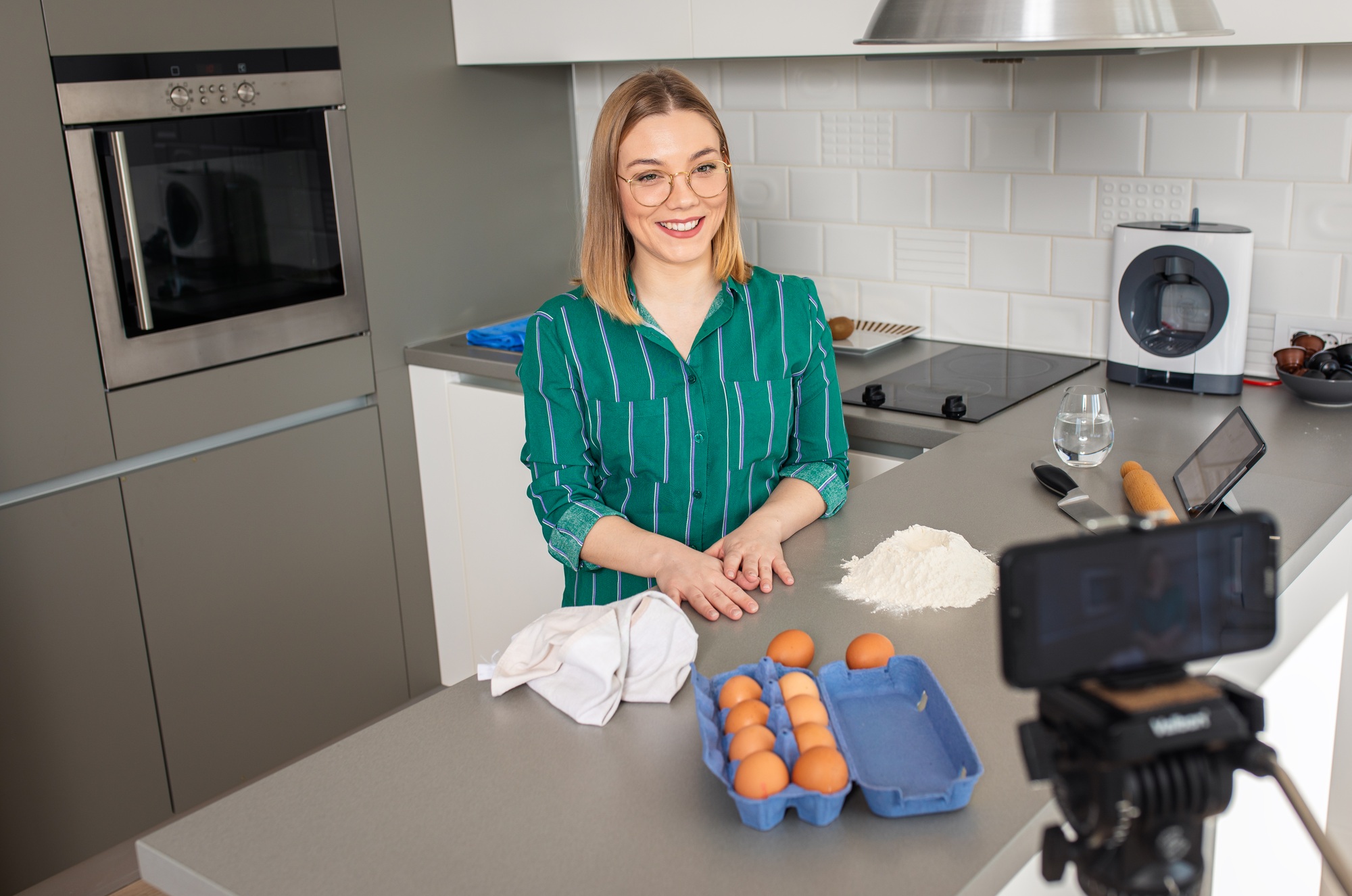 Young woman recording video blog with smart phone at home in kitchen making croissants.