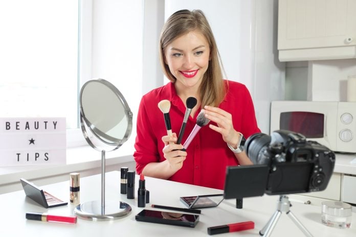 Young woman vlogger shows collection of three brushes, filming beauty vlog