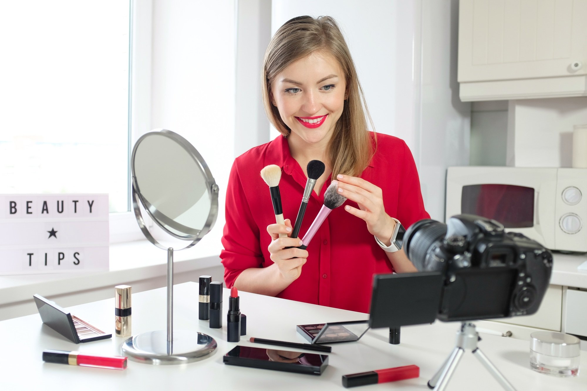 Young woman vlogger shows collection of three brushes, filming beauty vlog