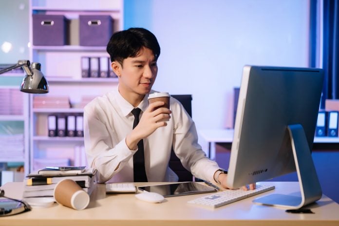Businessman drinking coffee to get some energy for working overtime sitting at desk using compute