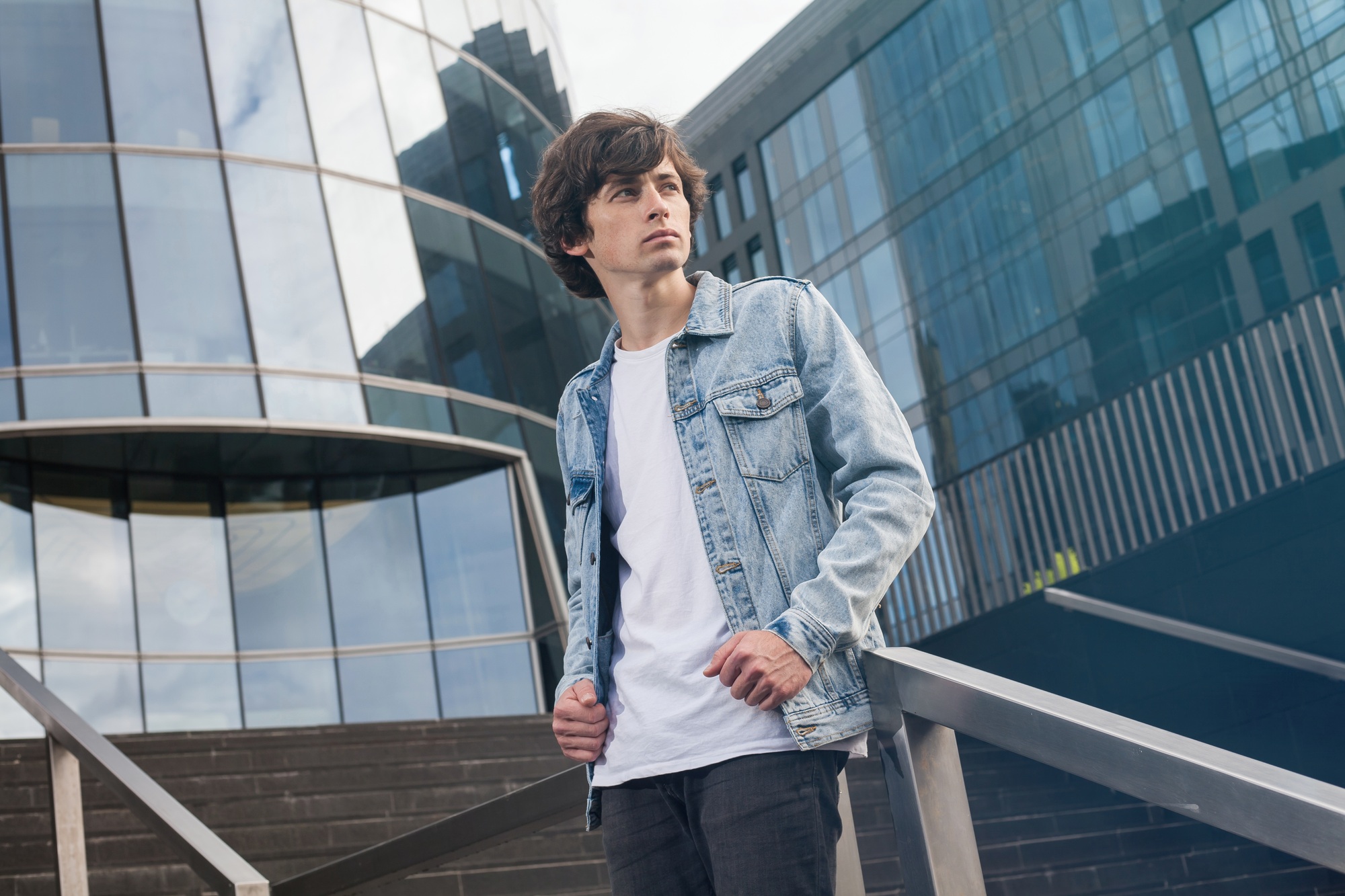 Attractive casual young student in jeans jacket standing on stairs