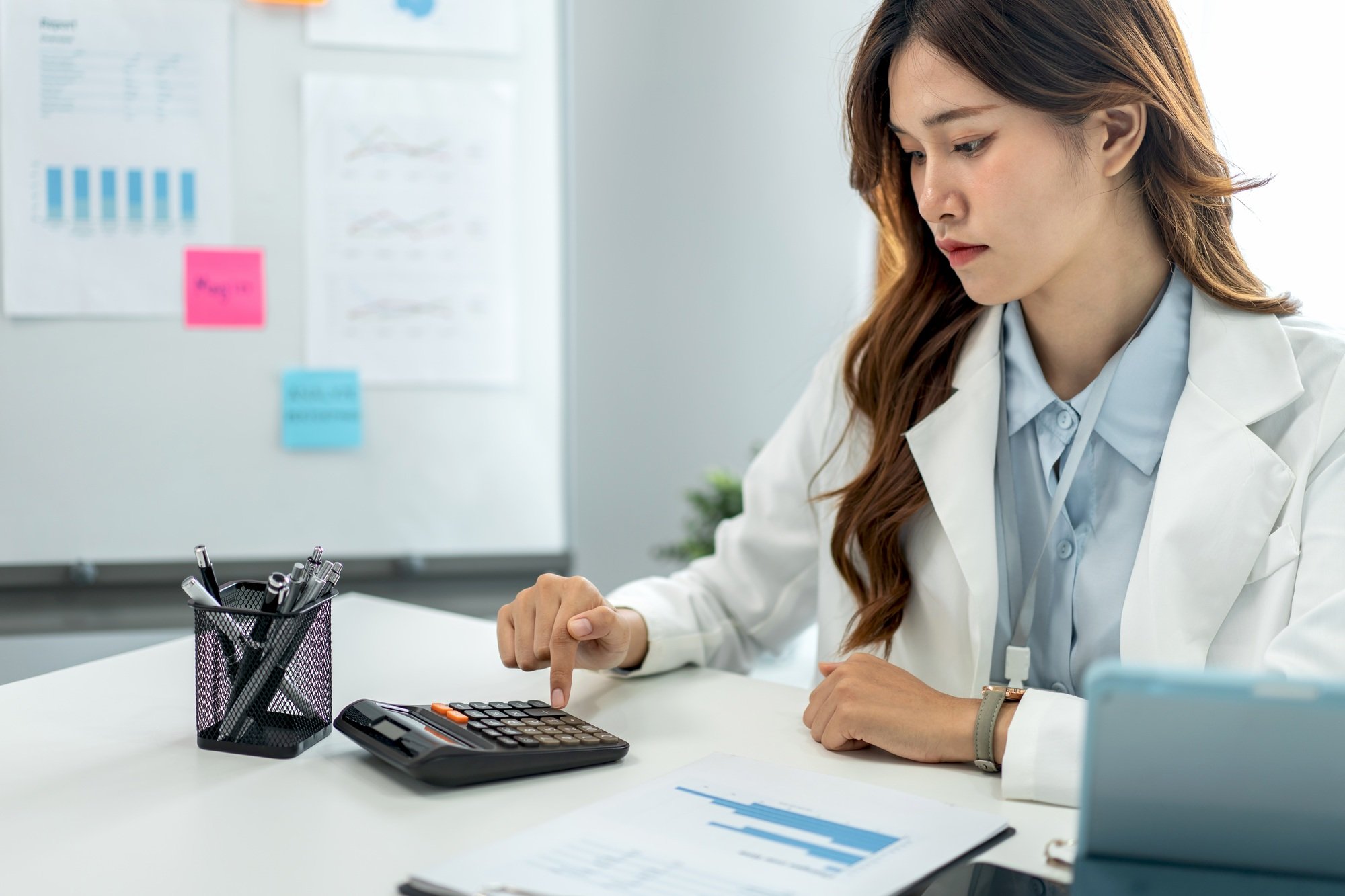 Businesswoman is using calculator to calculate cost and income of business while working to analysis
