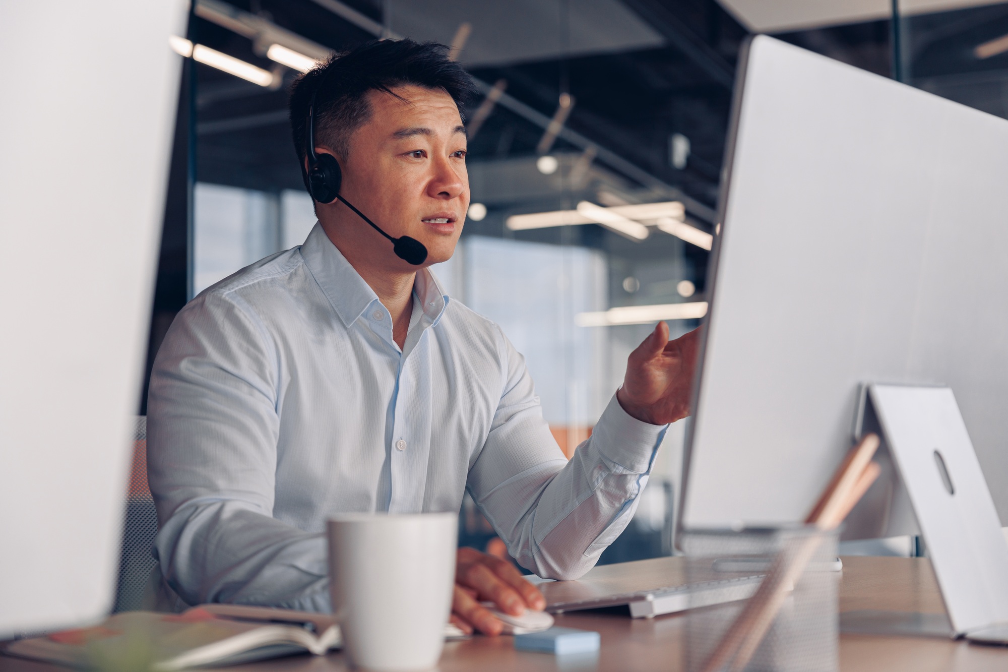 Focused asian businessman in headphones talking online with client sitting in office