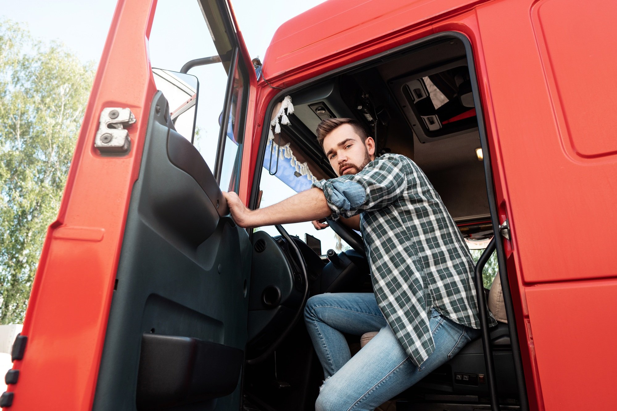 Handsome bearded truck driver inside his red cargo truck