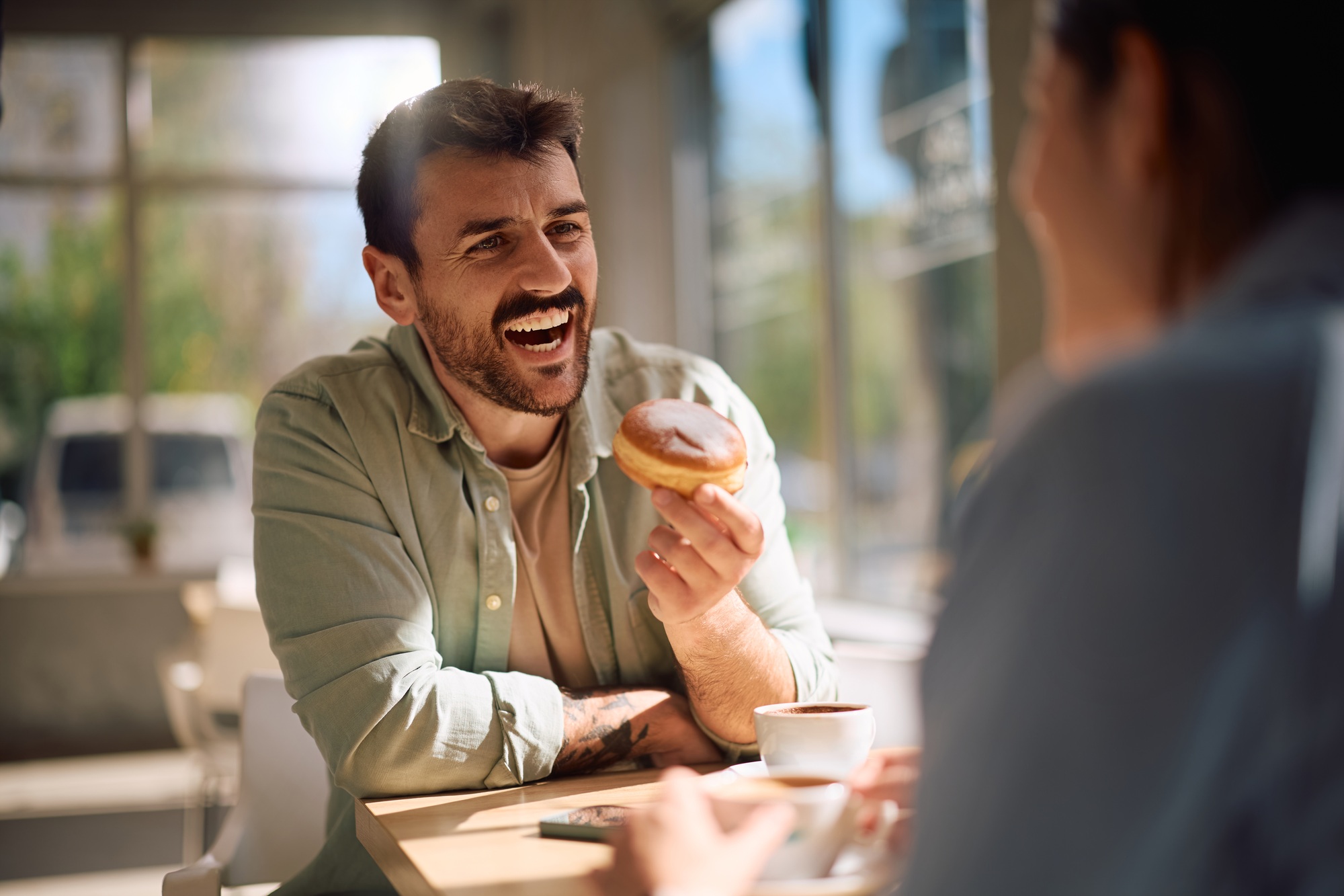 Happy man eating donut while talking to his girlfriend in a bakery shop.