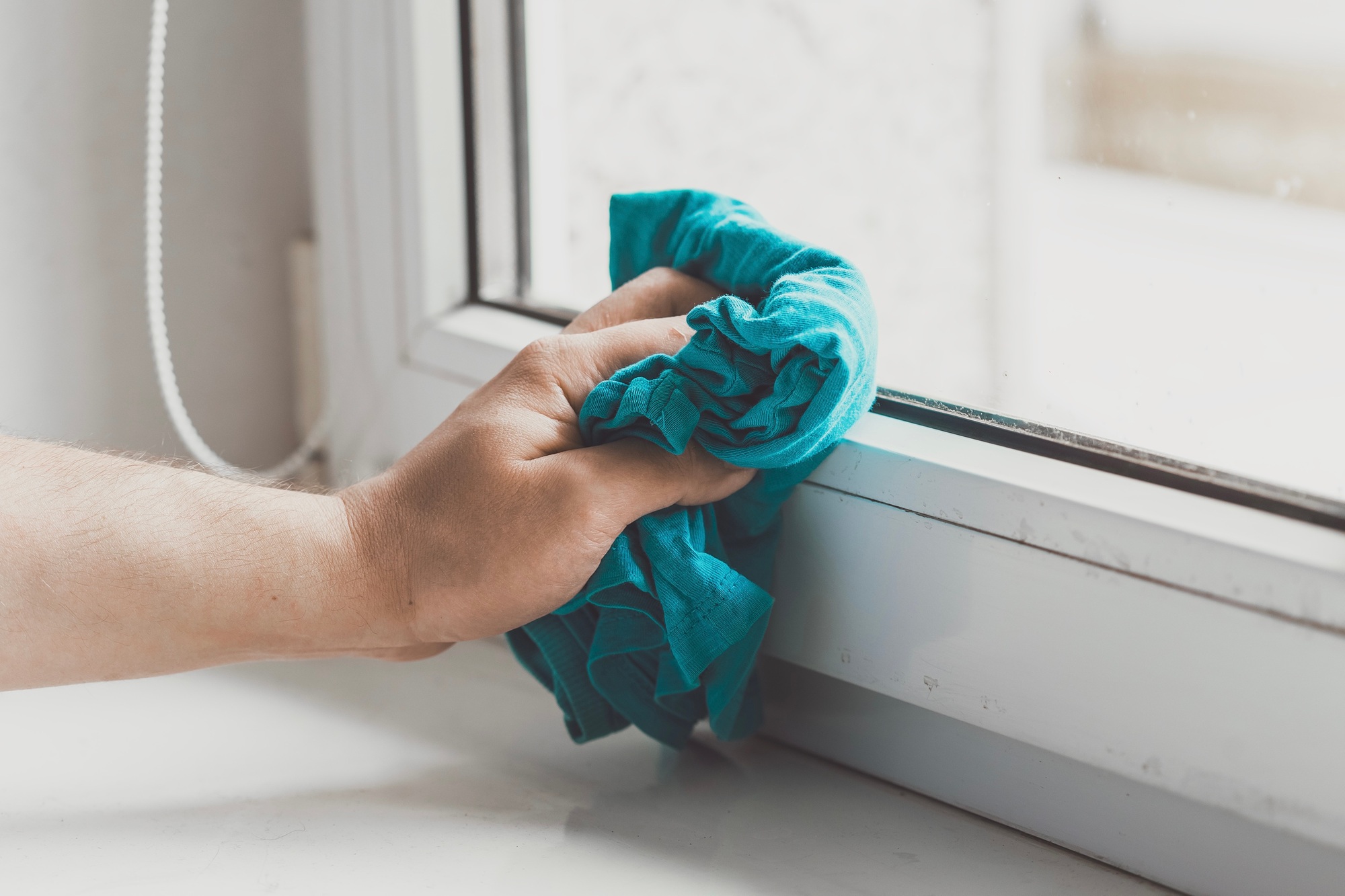 Man doing chores. Man’s hand cleaning windowsill with blue rug.