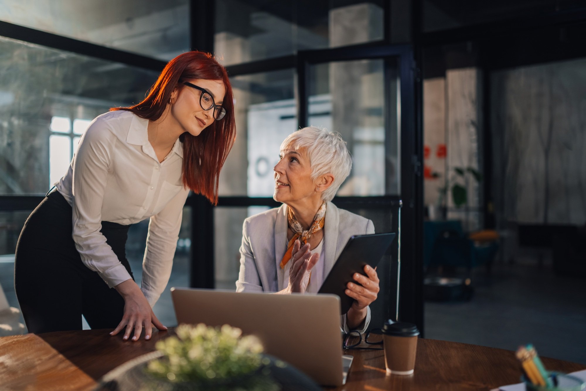 Mature female director with tablet discussing report with businesswoman