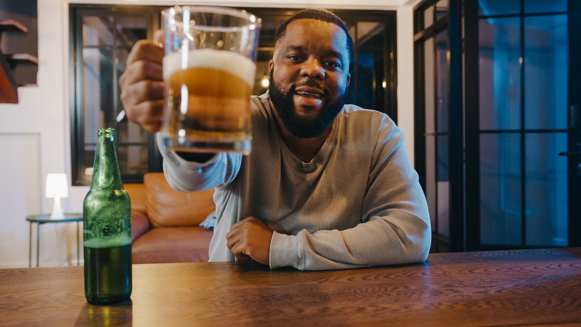 Middle-aged African American male drinking beer event online celebration via video call at home.