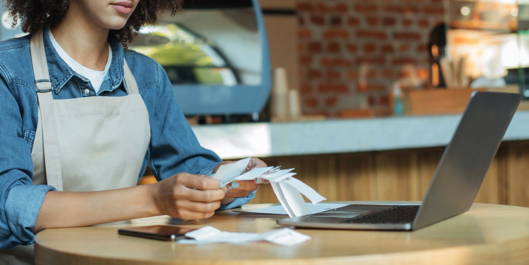 Millennial african american woman owner manager in apron works with account and bookkeeping in cafe