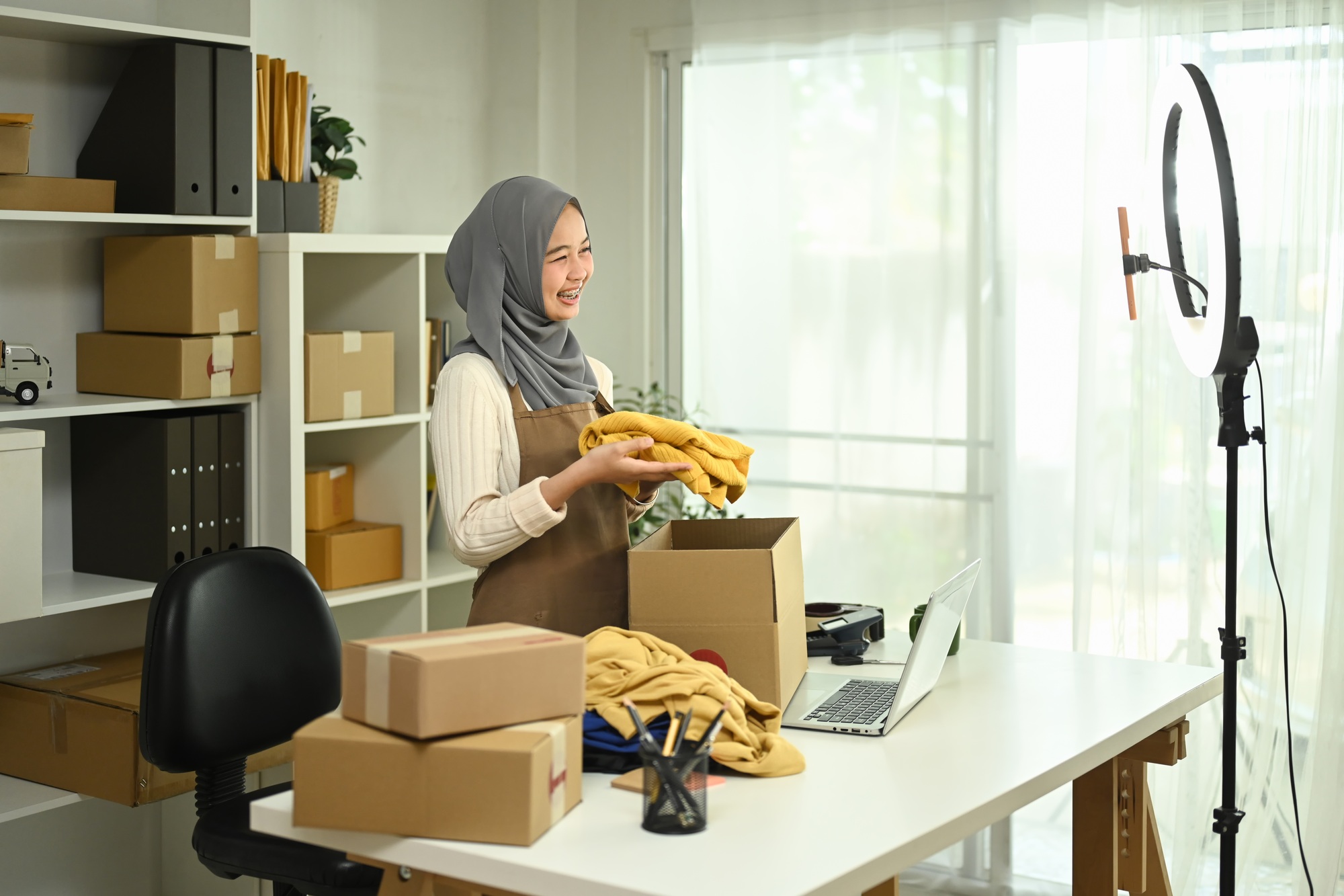 Smiling small business owner preparing parcel boxes of product and live streaming at home