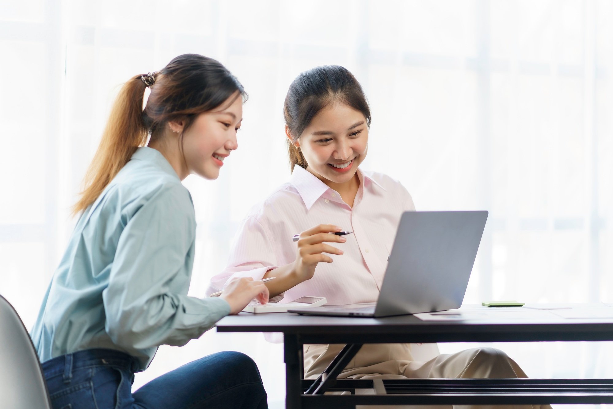 Two young beautiful Asian business woman in the conversation, exchanging ideas on laptop computer