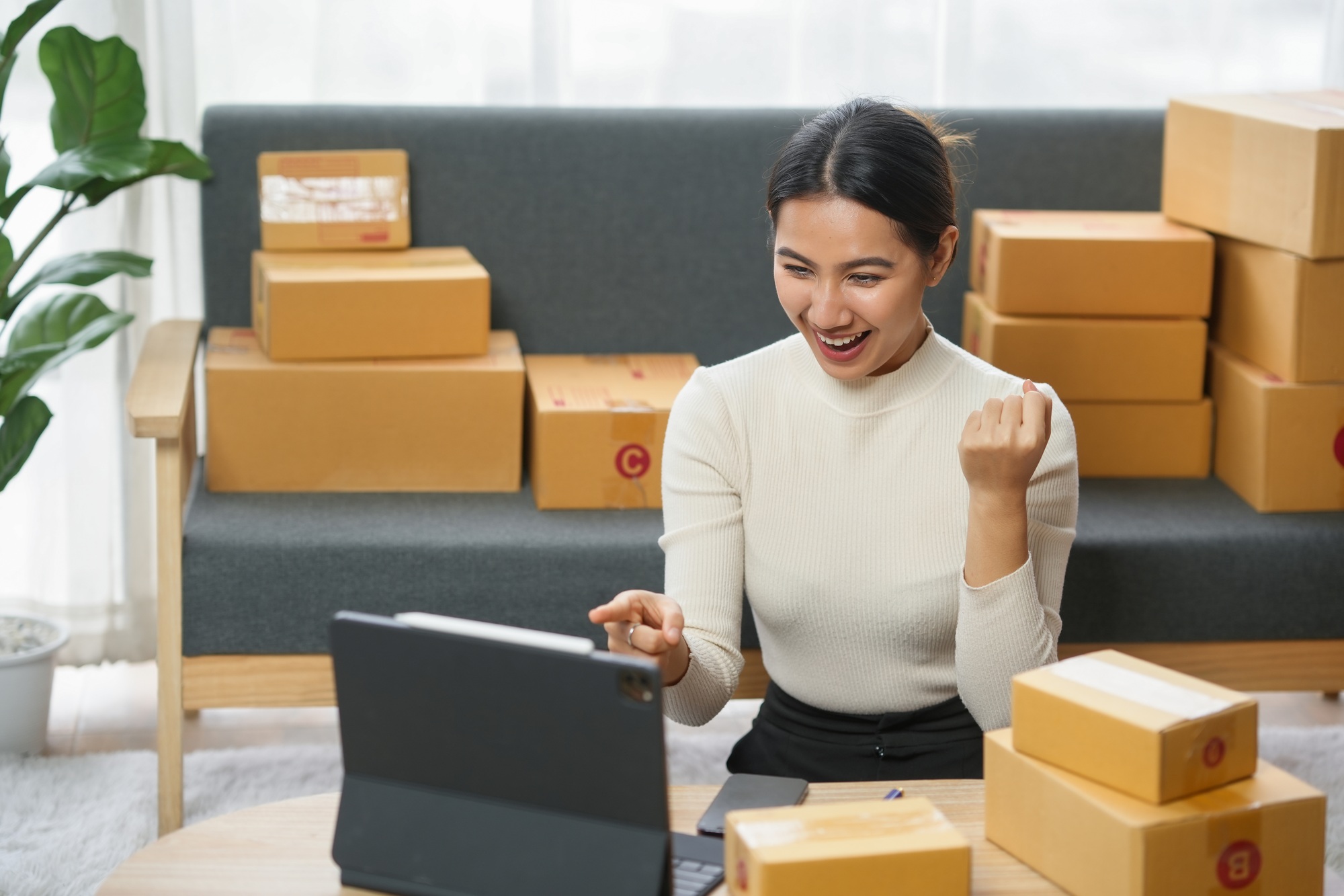 Woman celebrating online sales success with laptop and shipping boxes.