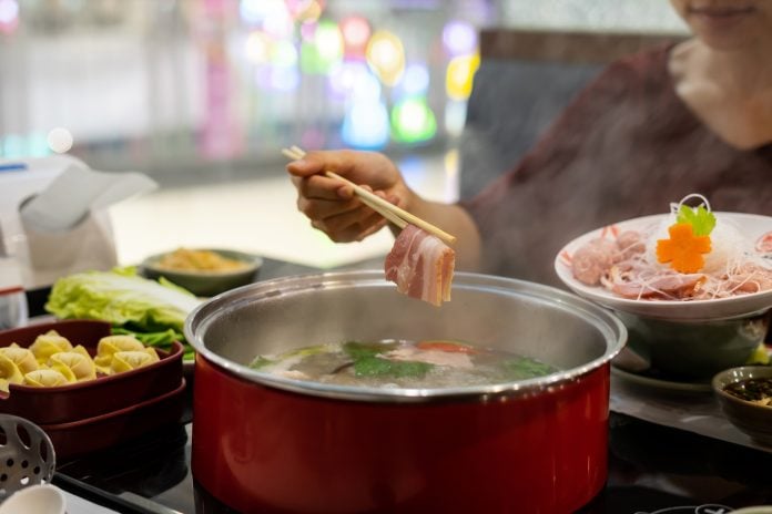 Young woman enjoy eating sukiyaki in hot pot at restaurant