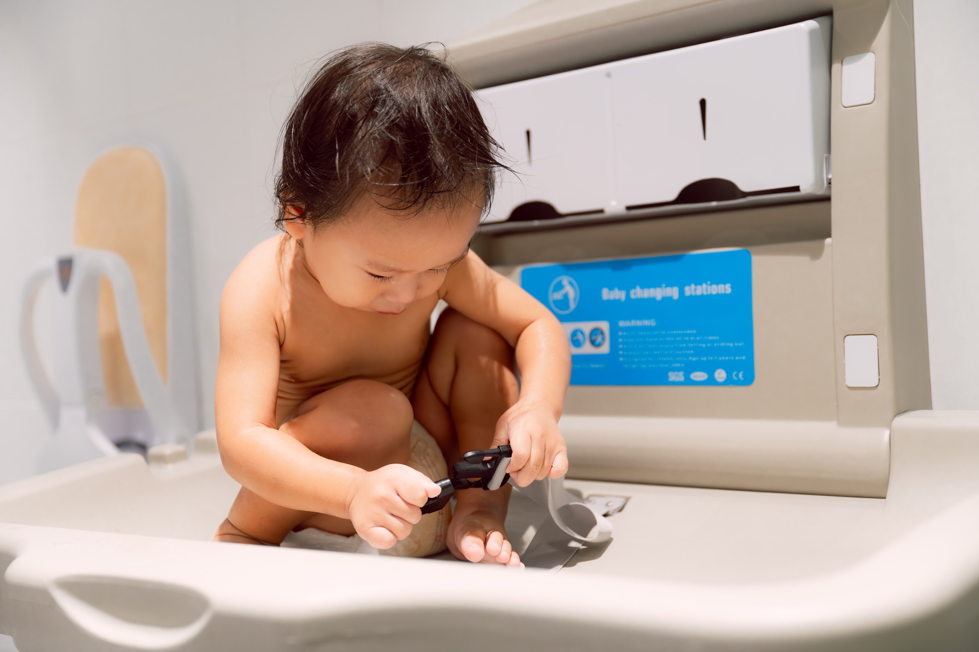 A boy is sitting at the Baby Changing Station waiting to be changed.