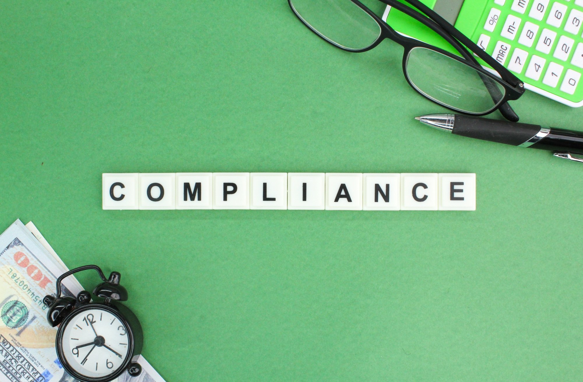 a calculator, glasses, banknotes and an alarm clock with the word compliance.