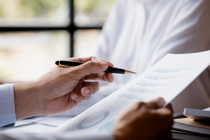 A close-up view of a businessman holding a pen pointing at a bar chart on a company financial.