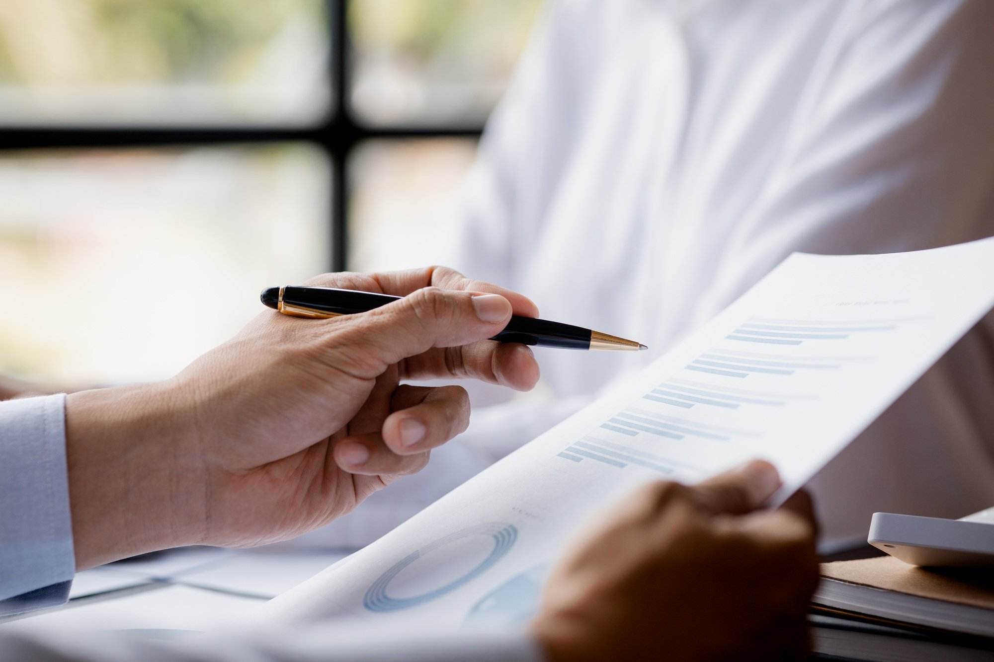 A close-up view of a businessman holding a pen pointing at a bar chart on a company financial.