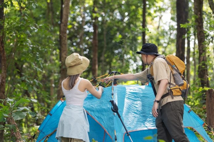 A couple sets up a blue tent in the middle of a dense forest