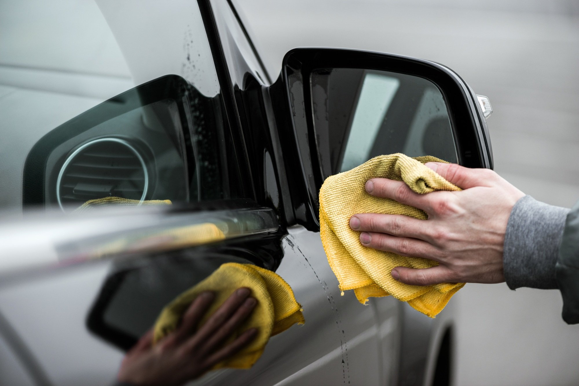 A man cleaning car's mirror with microfiber cloth, car detailing concept.