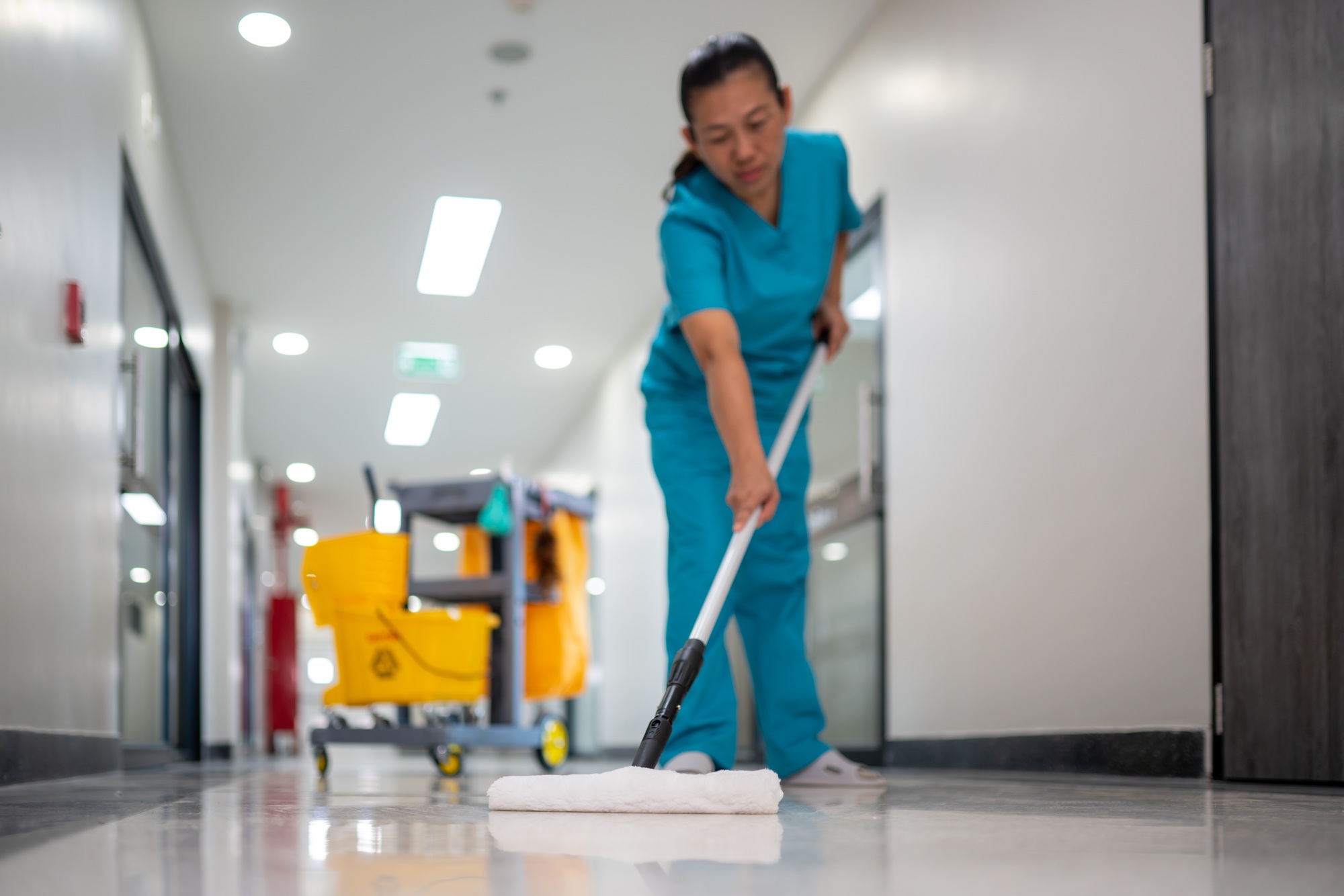 A woman in a blue scrub suit is mopping a floor